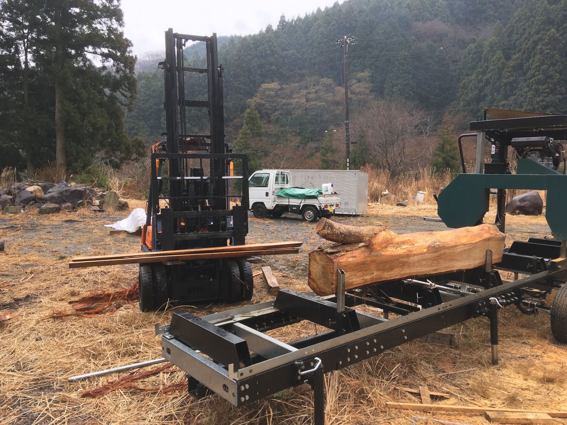 雨の日の土場。フォークリフトと、丸太を載せた移動式製材機