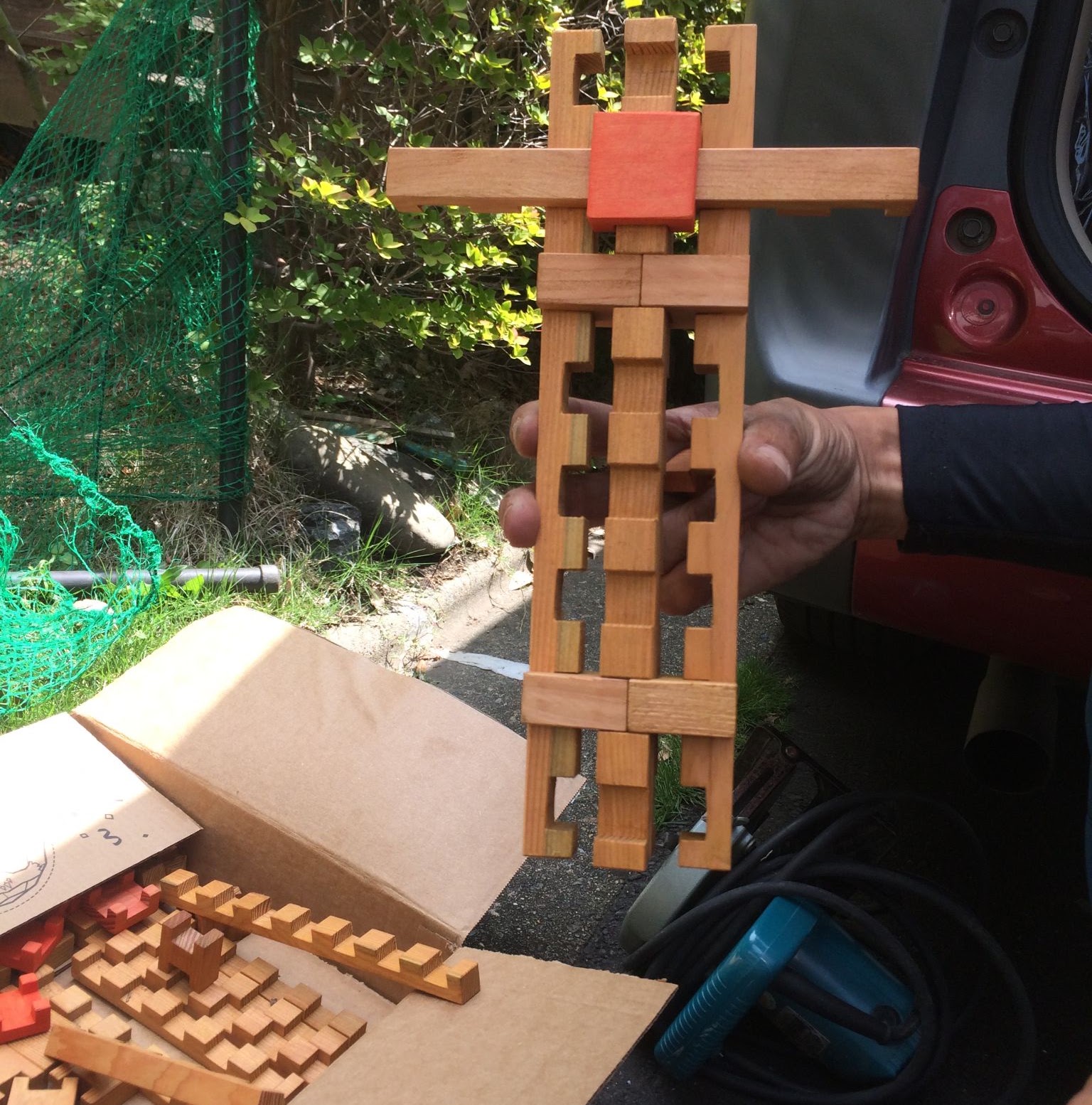 組木のブロックで作った人形を手に持った写真。手前の段ボール箱にもブロックが入っている